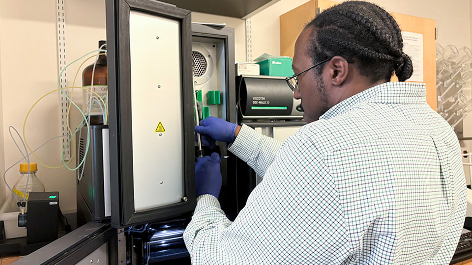 A researcher wearing gloves adjusting components inside a biopolymer processing instrument.