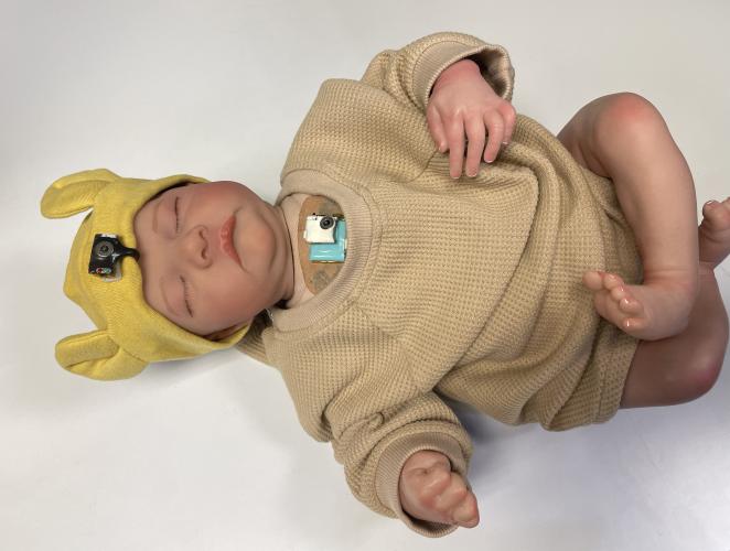 Wearable chest-mounted patch and forehead-mounted pulse oximeter shown on a mannequin baby for illustration